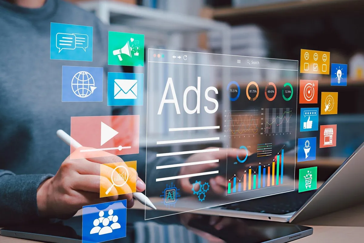 A creator working on a tablet and laptop with advertising layouts, charts and media icons floating above