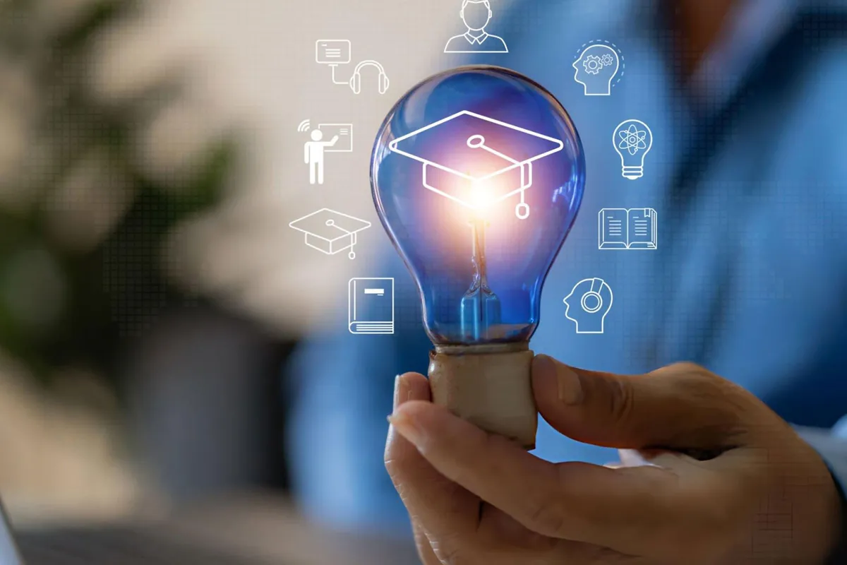 A hand holding a glowing light bulb with a graduation cap and learning icons
